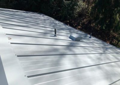 A white metal roof in a wooded area, installed by a professional roofing company.