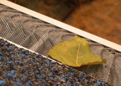 A leaf resting on a metal grate near a residential roofing.