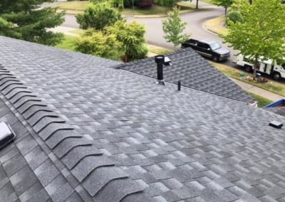 A gray shingled roof in a residential neighborhood, showcasing the excellent craftsmanship of a roofing contractor.