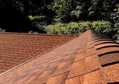 A brown shingled roofing contractor with trees in the background.