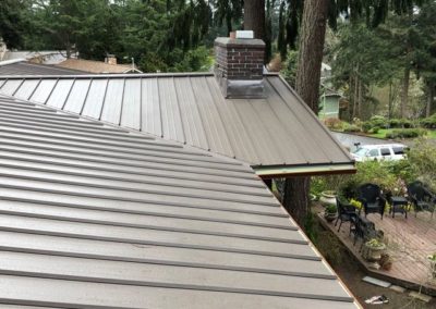 A residential metal roof installation atop a house with trees in the background.